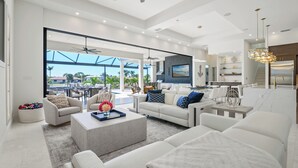A spacious living room with a large window, a ceiling fan, and a modern kitchen area.