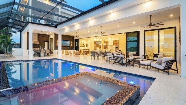 A modern indoor pool area with a glass ceiling, multiple seating areas, and a dining space.