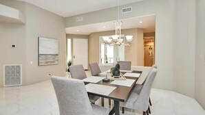 A modern dining room with a rectangular table, grey upholstered chairs, and a chandelier.