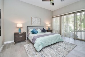 A bedroom with a bed, nightstands, a lamp, a painting, and a view through a window.