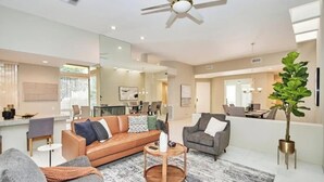 A modern living room with a sofa, armchairs, a coffee table, and a dining area in the background.