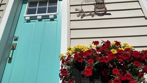 Una porta verde acqua con una finestra sopra, un cartello di benvenuto con un gufo e una fioriera con fiori rossi e gialli.