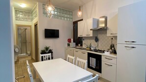 Una cuina moderna amb armaris blancs, una taula de dinar amb cadires i il·luminació penjant.