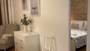 Un dormitori amb un llit, una cadira, un armari i una taula petita amb una planta.