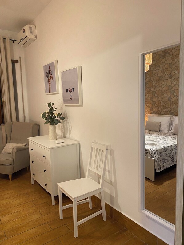 A bedroom with a bed, a chair, a dresser, and a small table with a plant.