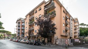 Un edifici d'apartaments de diversos pisos amb balcons, cotxes aparcats i un arbre a la façana.