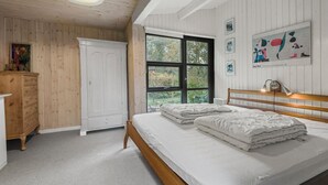A bedroom with a wooden wardrobe, a bed with white bedding, a window with a view of greenery, and a wall with abstract art. - 3 bedroom awesome home in Rødvig Stevns (Rødvig Stevns)