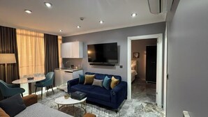 A modern living room with a sofa, a dining table, and a kitchen area with a flat-screen TV. - Viyana Suite Hotel (Istanbul)