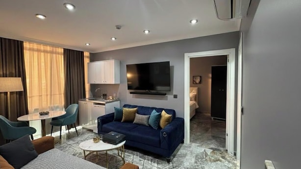 A modern living room with a sofa, a dining table, and a kitchen area with a flat-screen TV. - Viyana Suite Hotel (Istanbul)