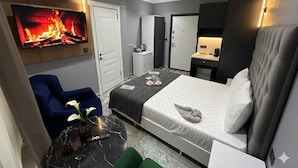 A modern hotel room with a large bed, a flat-screen TV mounted on the wall, a small seating area with a blue chair, and a marble-topped table. - Viyana Suite Hotel (Istanbul)