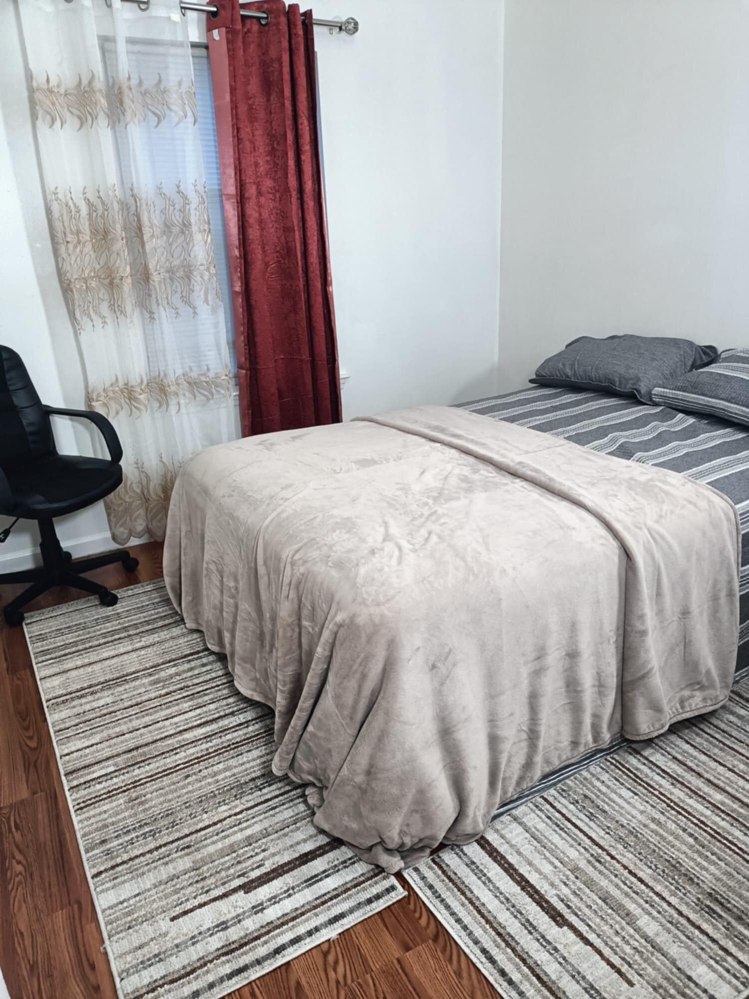 A bedroom with a bed, a chair, a rug, and curtains.