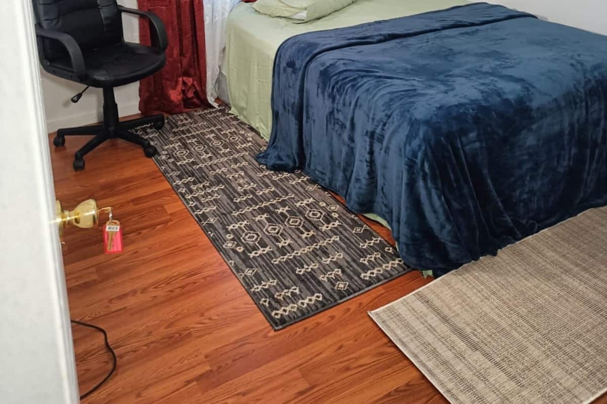 Ein kleines, ordentlich eingerichtetes Schlafzimmer mit einem Bett, einem Sessel und einem gemusterten Teppich.