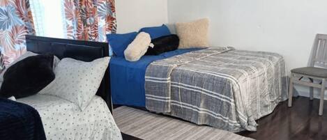 A room with two beds, a chair, a painting, and a window with curtains.