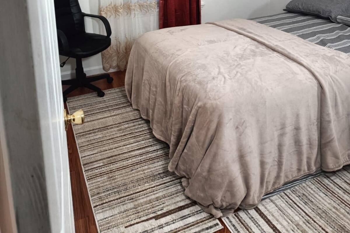 Ein Schlafzimmer mit einem Bett, einem Sessel, einem Fenster mit Vorhängen und einer Deckenleuchte.
