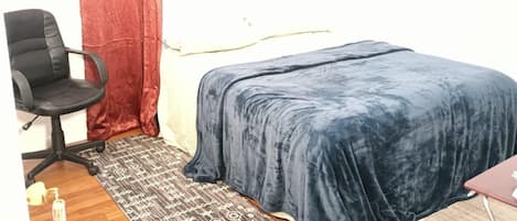Ein kleines Zimmer mit einem Bett, einem Sessel, einem Schreibtisch und einem Teppich.