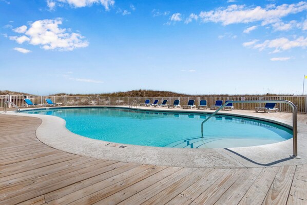 Ein Pool mit Holzterrasse, Liegestühlen und blauem Himmel.