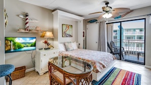 A bedroom with a bed, a TV, a ceiling fan, a balcony, and a view of a building. - Cozy Gulf-Side Studio Sugar Beach 235 (Orange Beach)