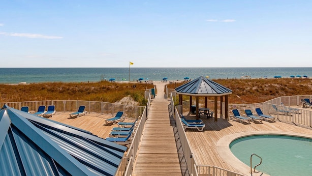 A wooden deck with lounge chairs and a pool, leading to a beach with umbrellas. - Cozy Gulf-Side Studio Sugar Beach 235 (Orange Beach)