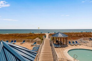 Eine Holzterrasse mit Liegestühlen und einem Pool, der zu einem Strand mit Sonnenschirmen führt.