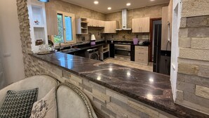 A modern kitchen with a central island, built-in appliances, and a stone accent wall. - 6-bedroom villa with pool & garden in palm hills-new cairo (Cairo Governorate)