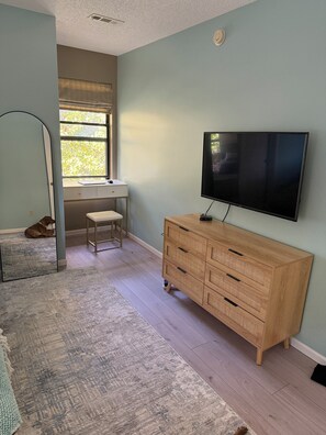 A room with a large flat-screen TV mounted on the wall, a wooden dresser, a desk with a chair, and a window with blinds. - 3-BR with lake views on Indian Point close to Silver Dollar City  (Branson)