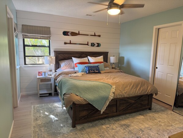A bedroom with a wooden bed, a window with blinds, a ceiling fan, and wall-mounted decorative items. - 3-BR with lake views on Indian Point close to Silver Dollar City  (Branson)