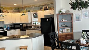 A modern kitchen with a central island, wooden bar stools, and a dining table with chairs.