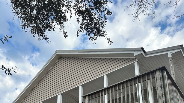 A two-story wooden house with a balcony, wooden deck, and outdoor seating area.