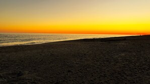 A beach at sunset with a clear sky and calm sea.