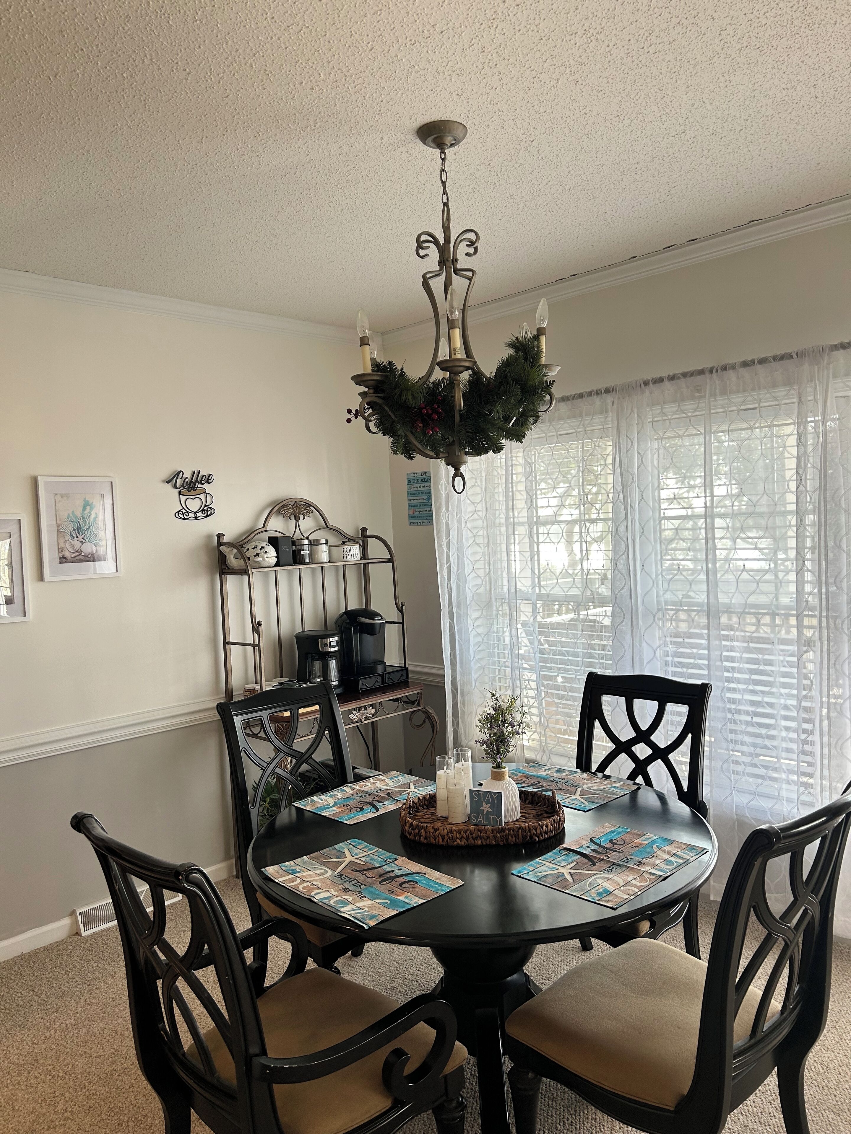 A dining area with a chandelier, a coffee station, and a table set for four with placemats and a centerpiece.