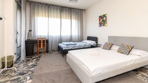 Una habitación de hotel con cama, escritorio, silla y ventana con cortinas.