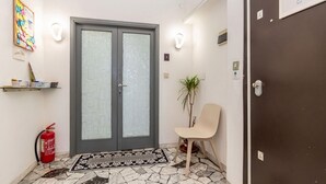 Pasillo con una puerta doble, un extintor, una silla, una planta en maceta y un cartel que indica cerrar la puerta al salir.