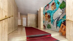 Una escalera de mármol con alfombra roja, barandilla y un mural en la pared.