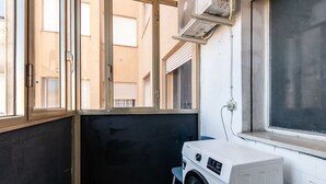 Un cuarto de lavandería con lavadora, una silla y una ventana con persianas.