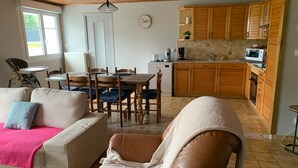 A living room with a sofa, a chair, a dining table with chairs, and a kitchen area with wooden cabinets and a microwave. - Maison Ty'Bell-At the gateway to the Gulf of Morbihan  (Moustoir-Ac)