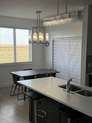 A modern kitchen with a central island, stainless steel sink, and pendant lighting. - Spacious 3 bedroom house with front attached garage (Regina)