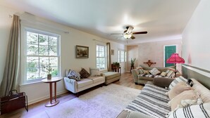 A spacious living room with a large window, a ceiling fan, and a cozy seating area with a sofa and armchairs.