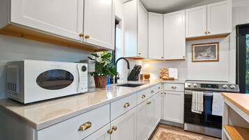 A modern kitchen with white cabinets, a built-in microwave, a stove, and a sink.