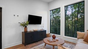 Un salon moderne doté d’une grande fenêtre, d’un téléviseur à écran plat, d’un meuble en bois foncé et d’une table basse ronde en bois.