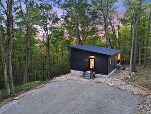 Une petite cabane à l’extérieur sombre, avec une porte d’entrée et un petit porche.