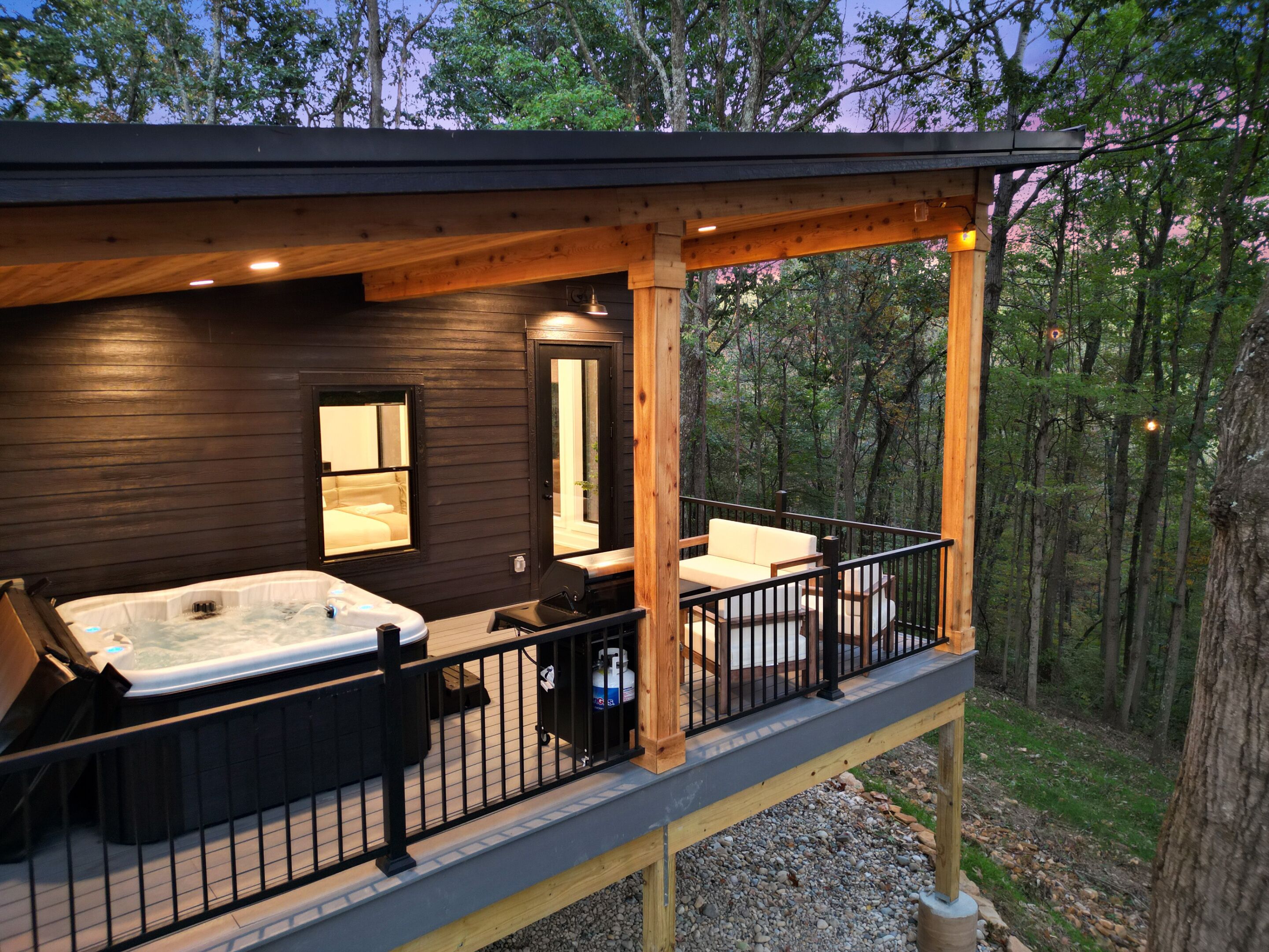 A wooden cabin with a hot tub, a sofa, and a balcony overlooking a forest.