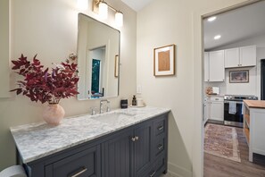 A modern bathroom with a marble sink, dark cabinets, a large mirror, and a potted plant. - Thompson Oasis | Hocking Hills, Romantic Cabin (Laurelville)