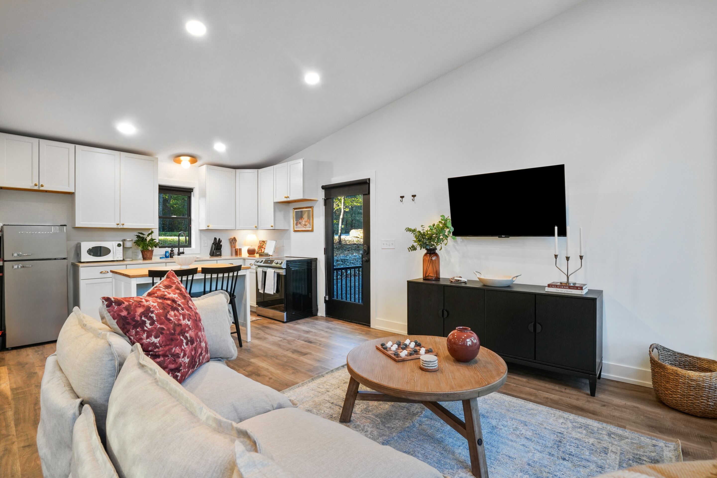 A modern kitchen with white cabinets, a dining area with a round table, and a living room with a sofa.
