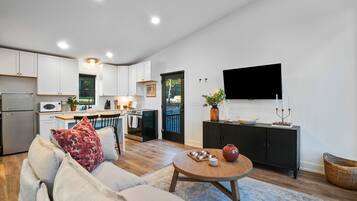 A modern kitchen with white cabinets, a dining area with a round table, and a living room with a sofa.