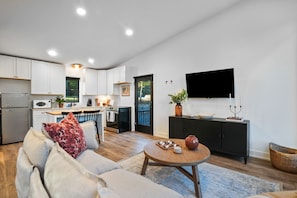 A modern kitchen with white cabinets, a dining area with a round table, and a living room with a sofa. - Thompson Oasis | Hocking Hills, Romantic Cabin (Laurelville)