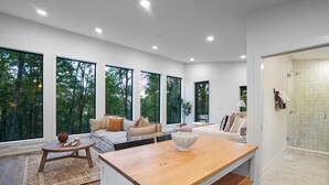 A modern interior with large windows, a wooden dining table, and a glass shower area.