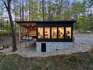 Une cabane moderne, dotée de fondations en pierre et de grandes fenêtres, entourée d’une forêt.