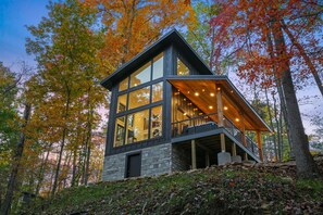 Eine moderne Holzhütte mit großen Fenstern, einer Holzterrasse und einem Steinfundament.