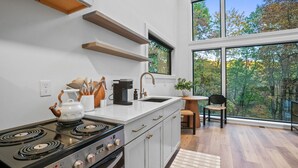 A modern kitchen with a stove, sink, and wooden shelves.