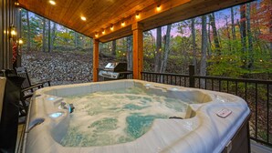 A hot tub under a wooden deck with a view of a forest.